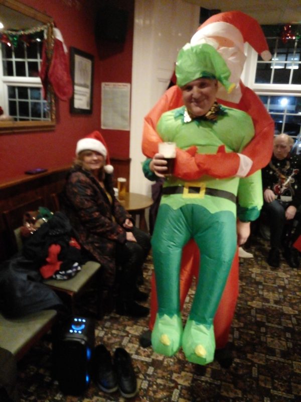 JULIE IN THE BACKGROUND AND JOHN THE ELF BEING HELD BY FATHER CHRISTMAS