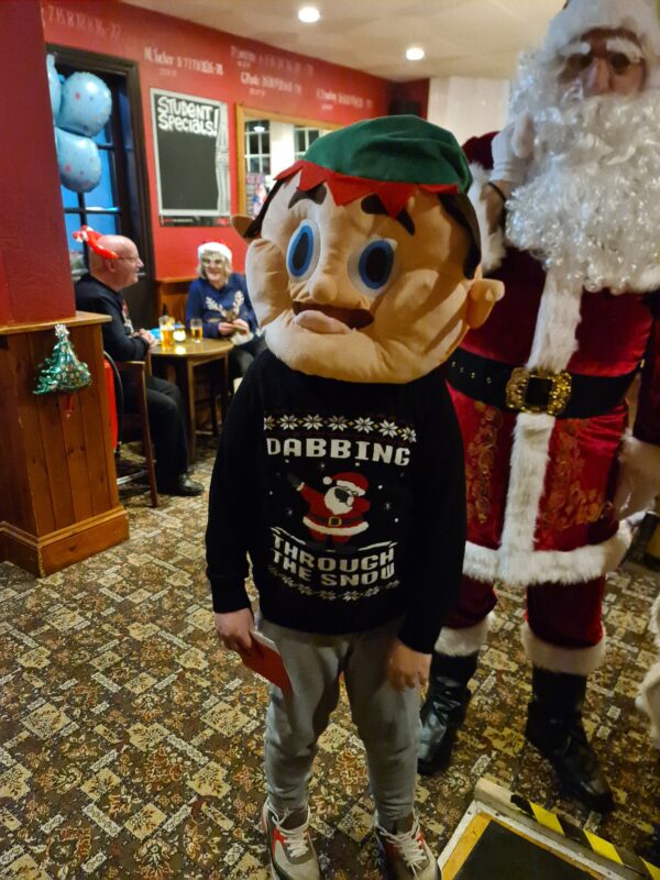 FATHER CHRISTMAS AND SAM WEARING A HUGE ELF MASK, WITH DAVID AND PAULINE TO THE LEFT OF THE PHOTO